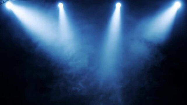 Multiple blue spotlights pierce through dark stage space, creating dramatic beams against black background filled with rising smoke.
