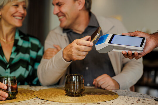 Senior man using smartphone to pay in restaurant