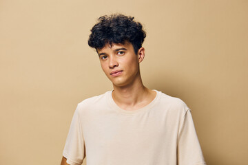 Young man with curly hair in a neutral beige background, looking confidently at the camera with a relaxed expression, showcasing casual attire and a natural pose