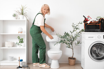 Mature female plumber fixing toilet bowl in bathroom