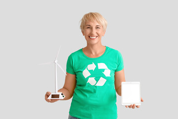 Mature woman with wind turbine model and tablet computer on light background