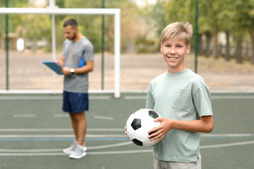 Happy boy with his dad playing football on soccer pitch