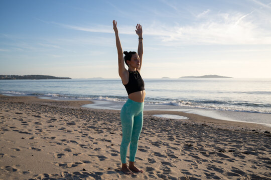 Yoga instructor practicing urdhva hastasana pose on the beach at sunrise
