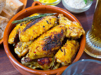Roasted chicken wings with golden crust served with mustard sauce and rosemary on clay bowl
