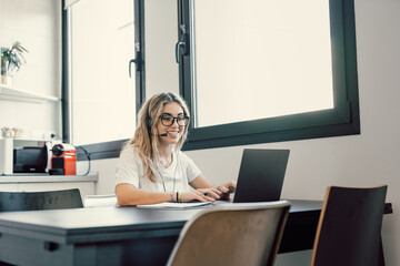 Happy millennial female in headphones watch webinar on laptop in modern office, smiling young businesswoman have fun laugh talk on video call with client or colleague use wireless Internet connection.