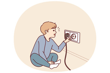 Small boy sticks fingers into socket, playing with electrical equipment and risking electric shock. Preschool child with curiosity pulls fingers to electrical socket and needs attention of parents