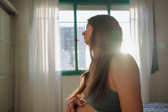 Pregnant Woman Sits by a Window, Bathed in Sunlight