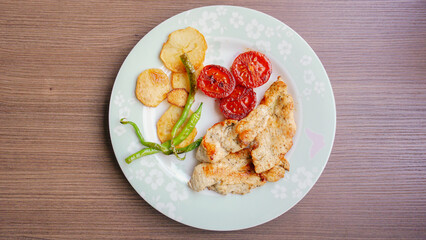 A delicious plate of grilled chicken served with roasted tomatoes, potatoes, and green peppers.