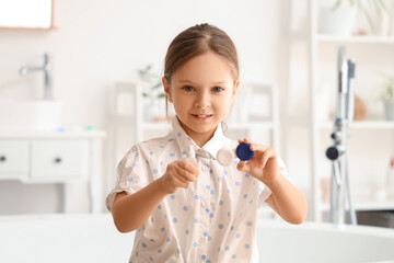 Cute little girl with contact lens case and bottle of solution in bathroom