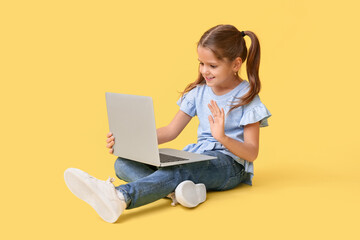 Happy little girl with laptop video chatting on yellow background