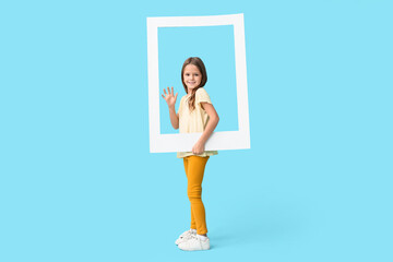 Happy little girl holding photo frame on blue background