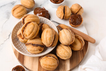 Bowl and cutting board of sweet walnut shaped cookies with boiled condensed milk on white background