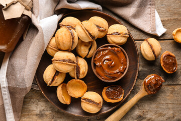 Plate with sweet walnut shaped cookies with boiled condensed milk on wooden background