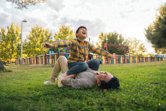 Child laughing while sitting on parent lying in the park