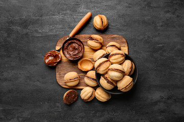 Wooden board and bowl of sweet walnut shaped cookies with boiled condensed milk on black background