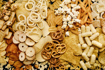 Colorful mix of salty snacks for beer varieties: chips and pretzels, onion rings and crackers. Non-healthy junk food background