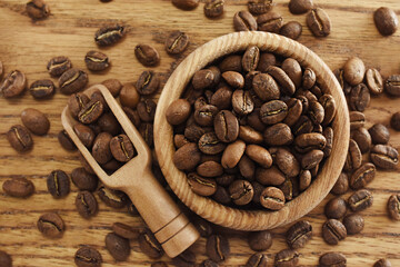 Roasted brown coffee beans in spoon on rustic wooden background, selective focus