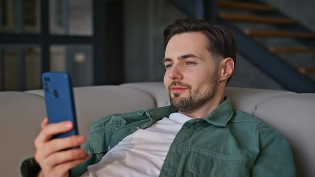 Lying guy typing smartphone couch looking screen at house environment closeup