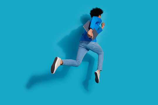 Full size photo of pretty young male running hurry netbook back view wear trendy outfit isolated on blue color background