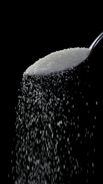 White sugar falling in slow motion on spoon on black background. Vertical video of 
