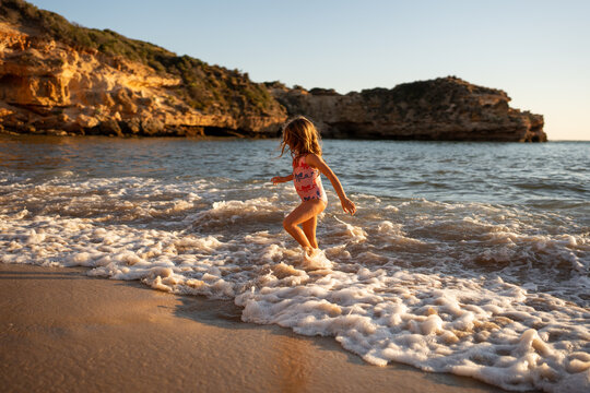 A little girl in the water on an empty beach at golden time.