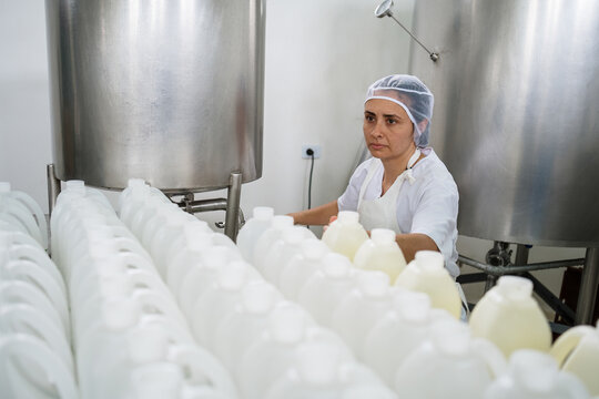 Female factory worker inspecting milk bottles on production line - Powered by Adobe
