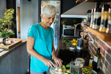 Senior woman adding protein powder to smoothie in kitchen for a healthy breakfast