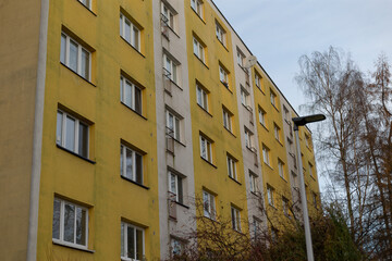 In a vibrant neighborhood, there stands a yellow building adorned with numerous windows, and a street light illuminates its entrance right in front of it