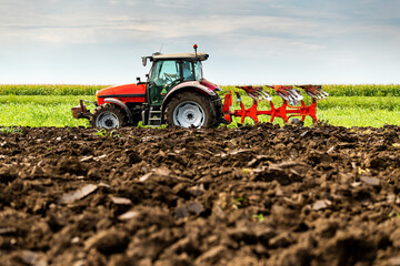 Obraz premium Tractor with plow attachment turns the soil in a vast, green farmland