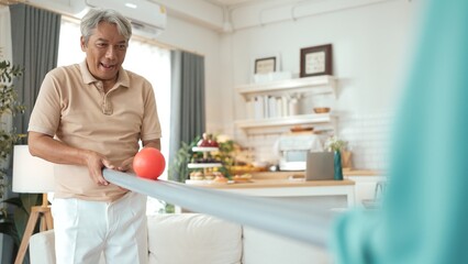 Elderly man playing a ball rolling game with his partner at home, practicing hand-eye coordination, focus, and motor skills for mental and physical wellness. Preventing healthcare concept. Myrmidon.