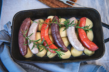 Close-up of bowl with raw homemade blood sausage, pork sausage and chorizo in oven with potatoes....