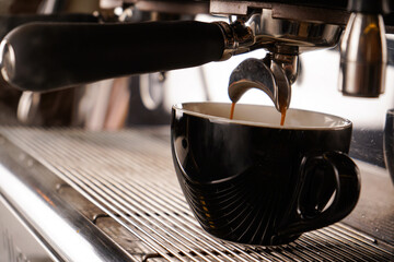 The work of a modern coffee machine in the process of preparing espresso in a black cup. A very aromatic drink.