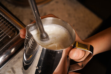 Steam frothing milk under the pressure of a coffee maker in a jug, close-up.