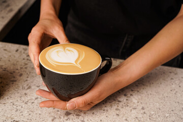 Top view of a cup of coffee with a drawn heart surrounded by a barista. Behind the bar.