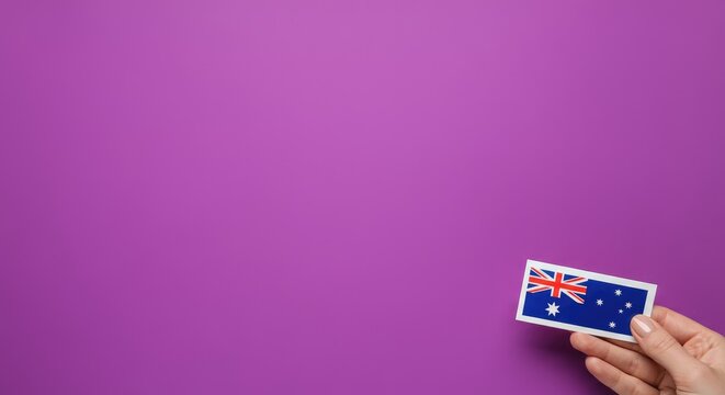 Hand holding small Australian flag sticker against purple background