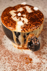 A rich cup of cocoa overflowing beyond the rim, topped with chocolate shavings, creates a mouthwatering sight of sweetness and indulgence.