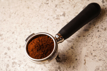 A side view of a porta filter filled with freshly ground coffee, next to a tamper, on a black background.