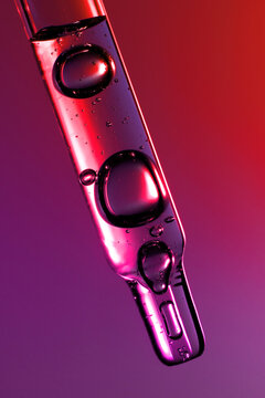 Clear glass pipette with face serum on purple red gradient background