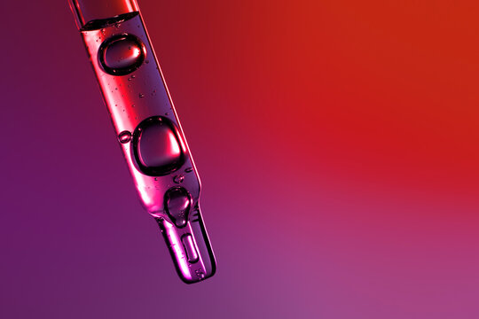 Clear glass pipette with face serum on purple red gradient background