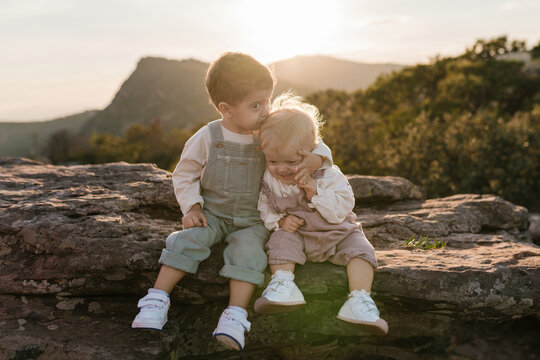 Big brother kissing baby sister at sunset