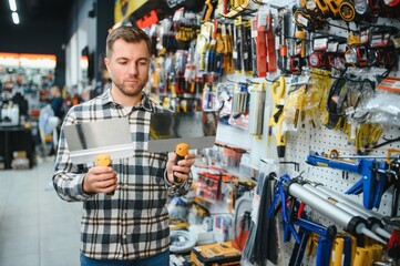 Fototapeta premium A male customer in a modern hardware store chooses trowels