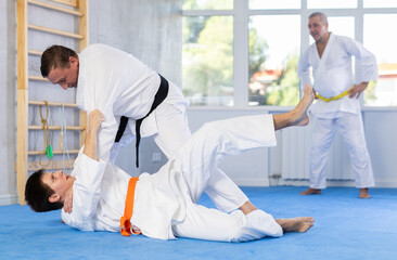 Obraz premium Concentrated karate sensei engaging kumite with young guy, working out fighting techniques in martial art training room..