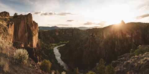 Obraz premium A dramatic canyon landscape with steep cliffs, a winding river below, and soft sunlight illuminating the rugged rocks. The powerful and timeless setting captures natureâ€™s grandeur.