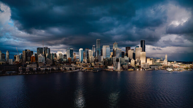 MAY 2024, SEATTLE, WASHINGTON, USA - stormy clouds over Seattle Skyline and Harbor with Ferris Wheel - sunset light hits buildings