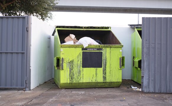 Green dumpster open in fenced enclosure waste management industry trash removal.