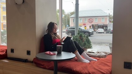 girl reading a book by the window sitting in a home cafe fixing her hair reading studying passing cars outside the window