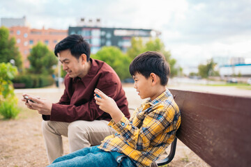 Father and son sitting on a bench playing video game on phone