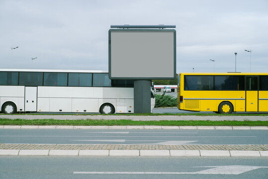 An empty billboard next to two buses 