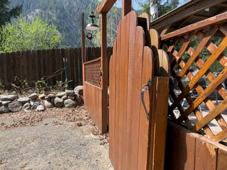 Beautiful view of an open wooden gate leading into a lush, green backyard on a sunny day