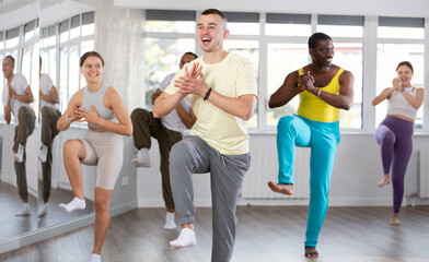Smiling active young man enjoying modern vigorous dance with multicultural mixed age group in modern fitness studio..
